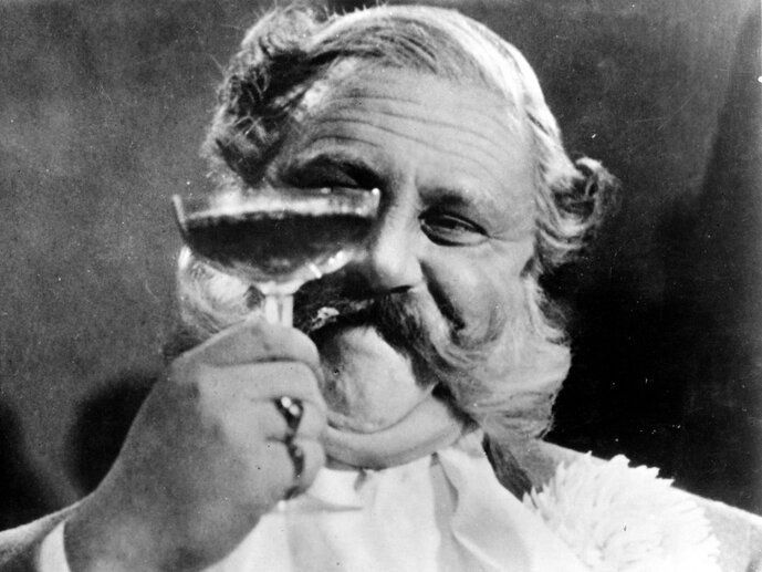 KI generiert: Ein Mann mit einem auffälligen Schnurrbart hält ein Glas Champagner hoch und scheint erfreut zu sein. Der Ausdruck in seinem Gesicht deutet auf Genuss und Zufriedenheit hin.