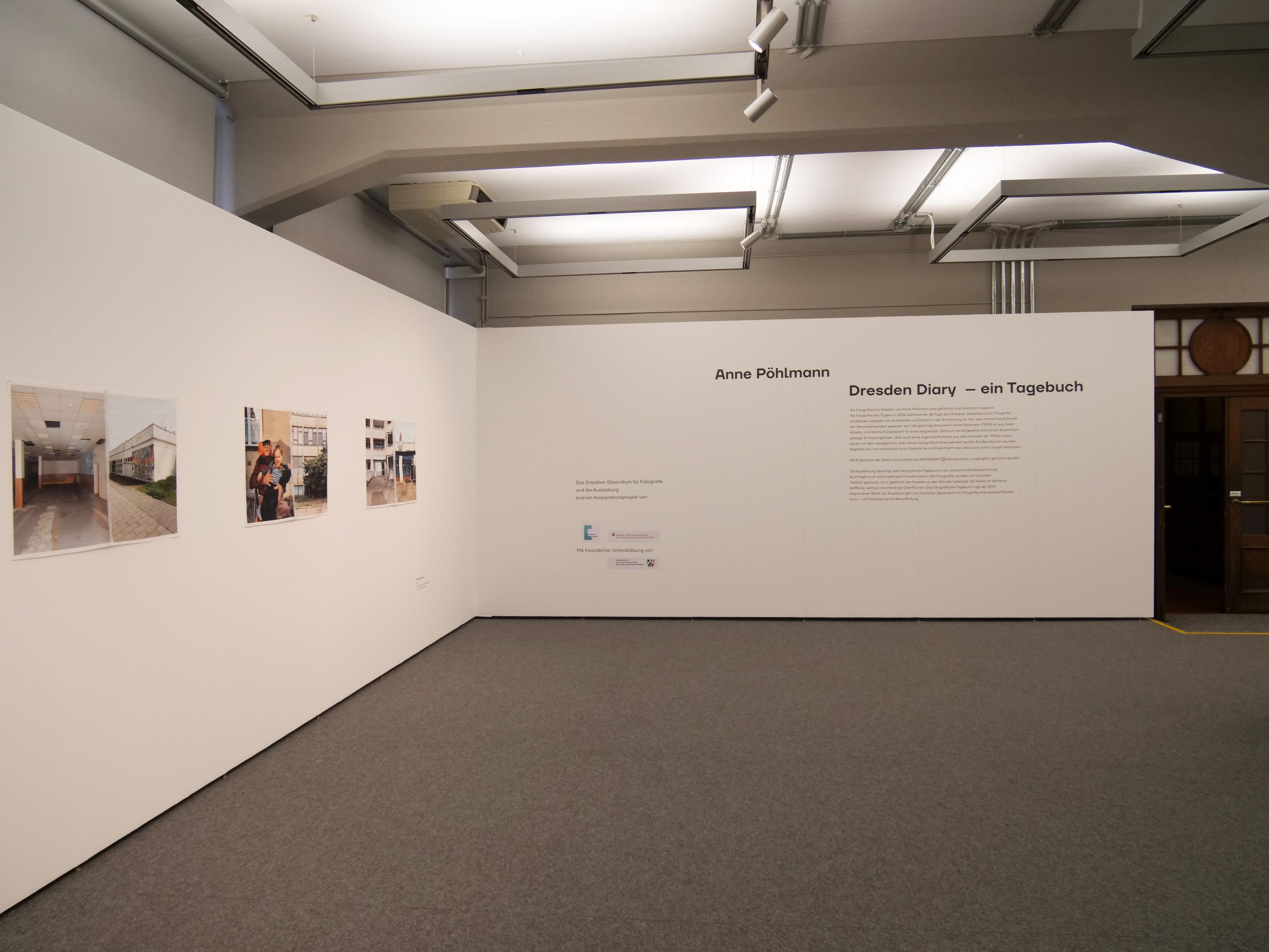 KI generiert: Das Bild zeigt einen Ausstellungsraum mit Fotografien an der Wand und dem Titel "Dresden Diary – ein Tagebuch" von Anne Pöhlmann. Der Raum ist minimalistisch gestaltet mit einem großen weißen Wandtext als Hauptfokus.