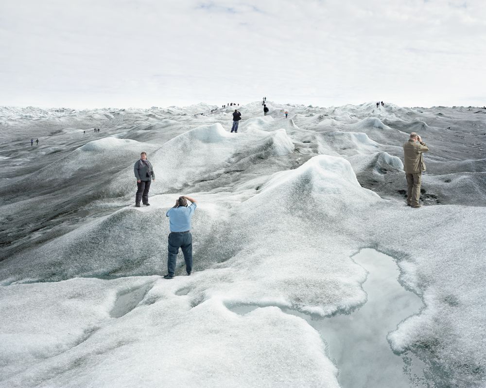 KI generiert: Das Bild zeigt mehrere Menschen, die auf einer eisigen, hügeligen Landschaft stehen und Fotos machen. Die Hauptinhalte des Bildes sind die Personen und die weite Eislandschaft.