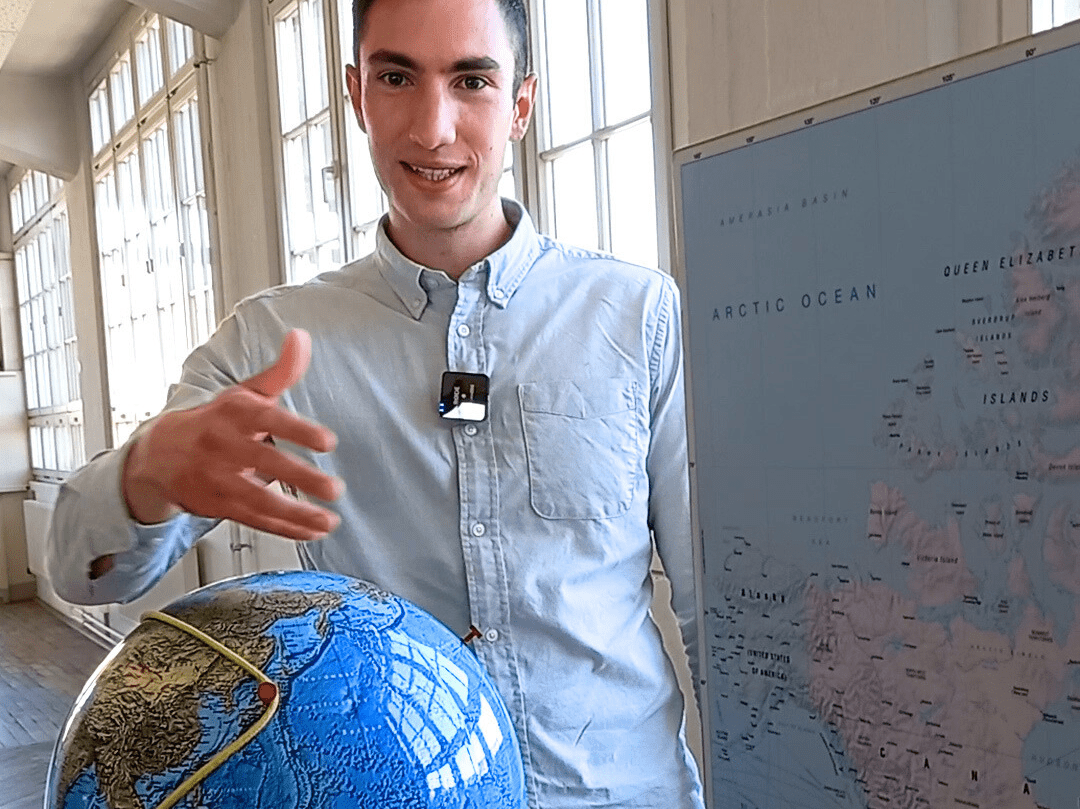 KI generiert: Ein Mann steht neben einem Globus und zeigt auf eine Weltkarte. Der Raum ist hell mit großen Fenstern.