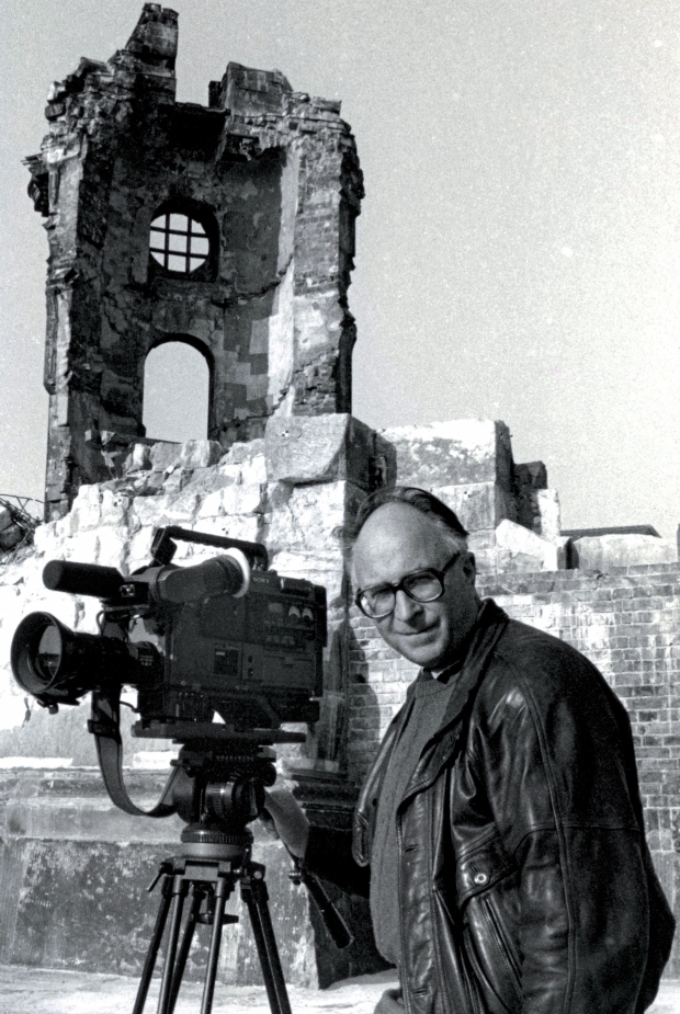 KI generiert: Das Bild zeigt eine Person mit einer Filmkamera auf einem Stativ vor den Ruinen eines Gebäudes. Der Fokus liegt auf der Kombination aus Filmproduktion und historischer Architektur.