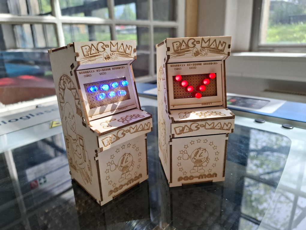 KI generiert: Das Bild zeigt zwei Miniatur-Arcade-Spielautomaten aus Holz mit dem Thema Pac-Man. Die Bildschirme sind mit blauen und roten LED-Lichtern ausgestattet, die Spielfiguren simulieren.