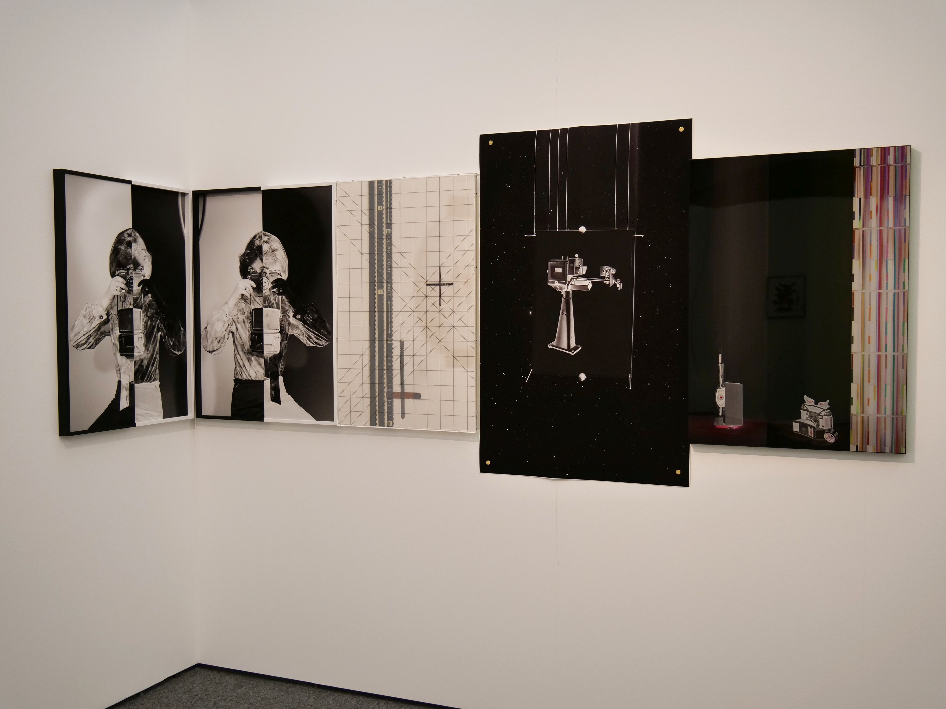 KI generiert: Das Bild zeigt eine Kunstinstallation, die aus mehreren an der Wand hängenden Tafeln besteht. Die Tafeln zeigen eine Mischung aus Schwarz-Weiß-Porträts, geometrischen Mustern und technischen Objekten.