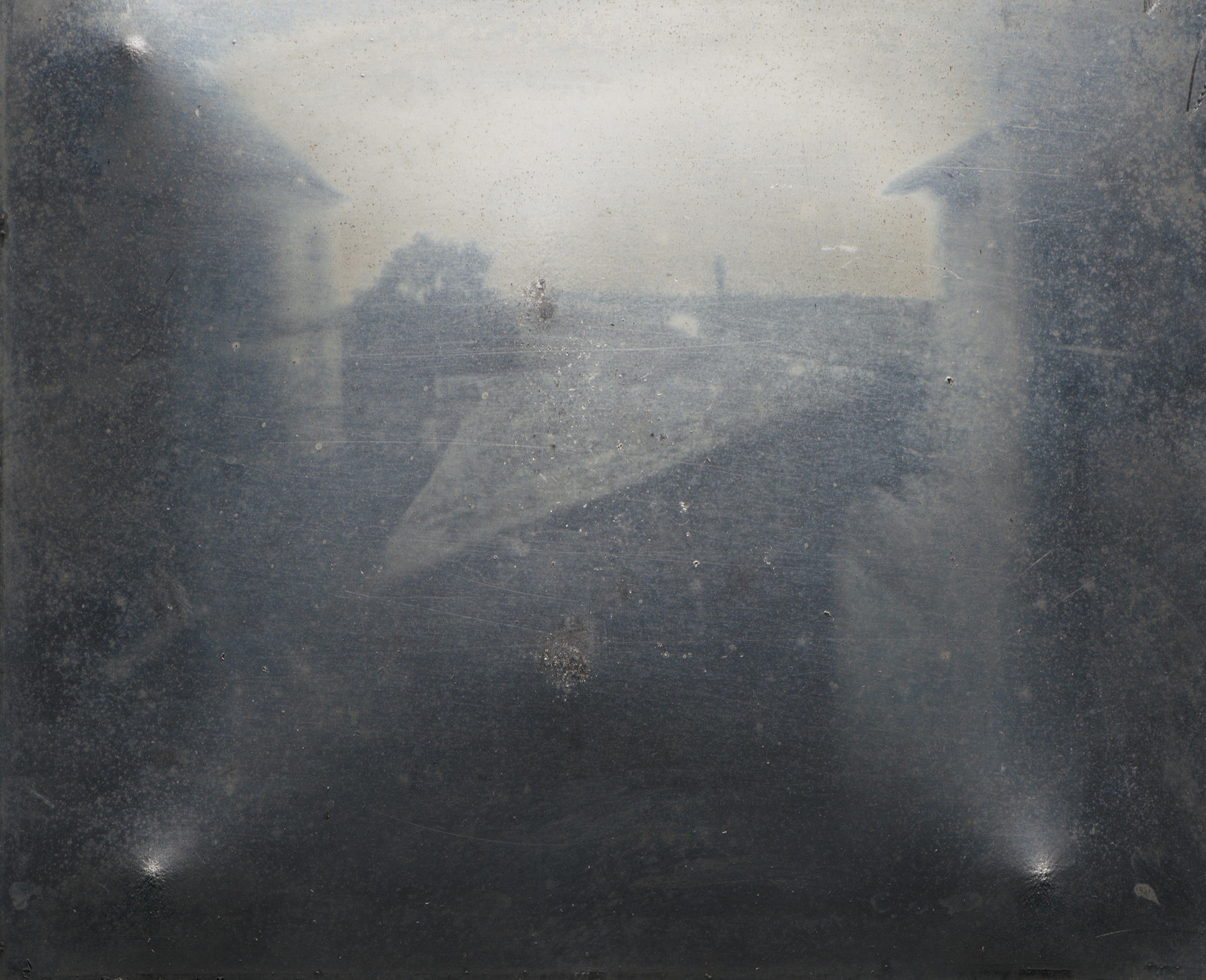 AI generated: The image shows a blurred view from a window with faintly recognisable structures, probably buildings or landscape. It is one of the earliest photographic images.
