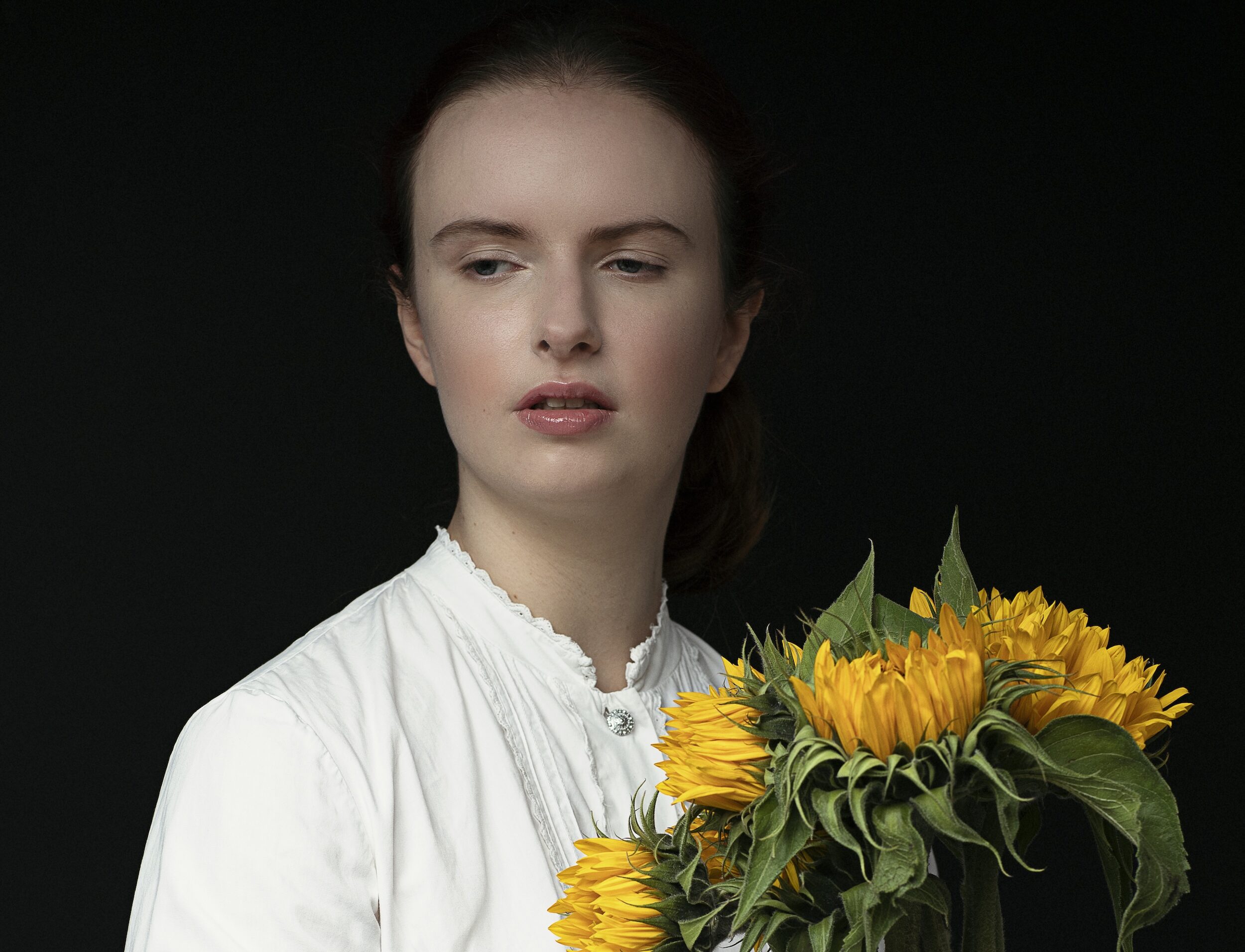 KI generiert: Das Bild zeigt eine Person in einem weißen Oberteil, die einen Strauß Sonnenblumen hält. Der Hintergrund ist dunkel, was die Aufmerksamkeit auf die Person und die Blumen lenkt.