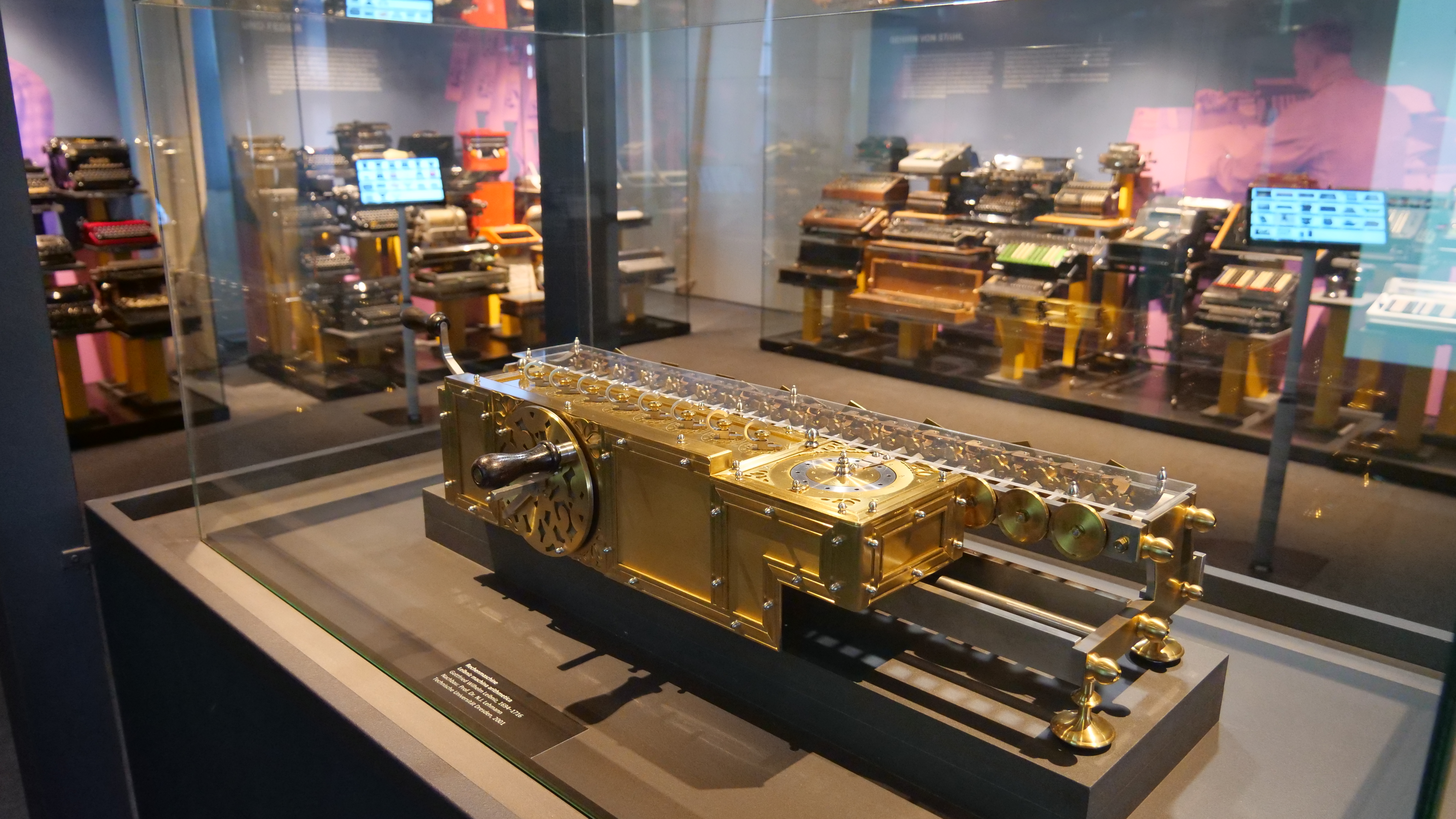 KI generiert: Das Bild zeigt eine Ausstellung von verschiedenen historischen Rechenmaschinen und mechanischen Geräten in einem Museum. Im Vordergrund befindet sich eine goldene Rechenmaschine in einer Glasvitrine.