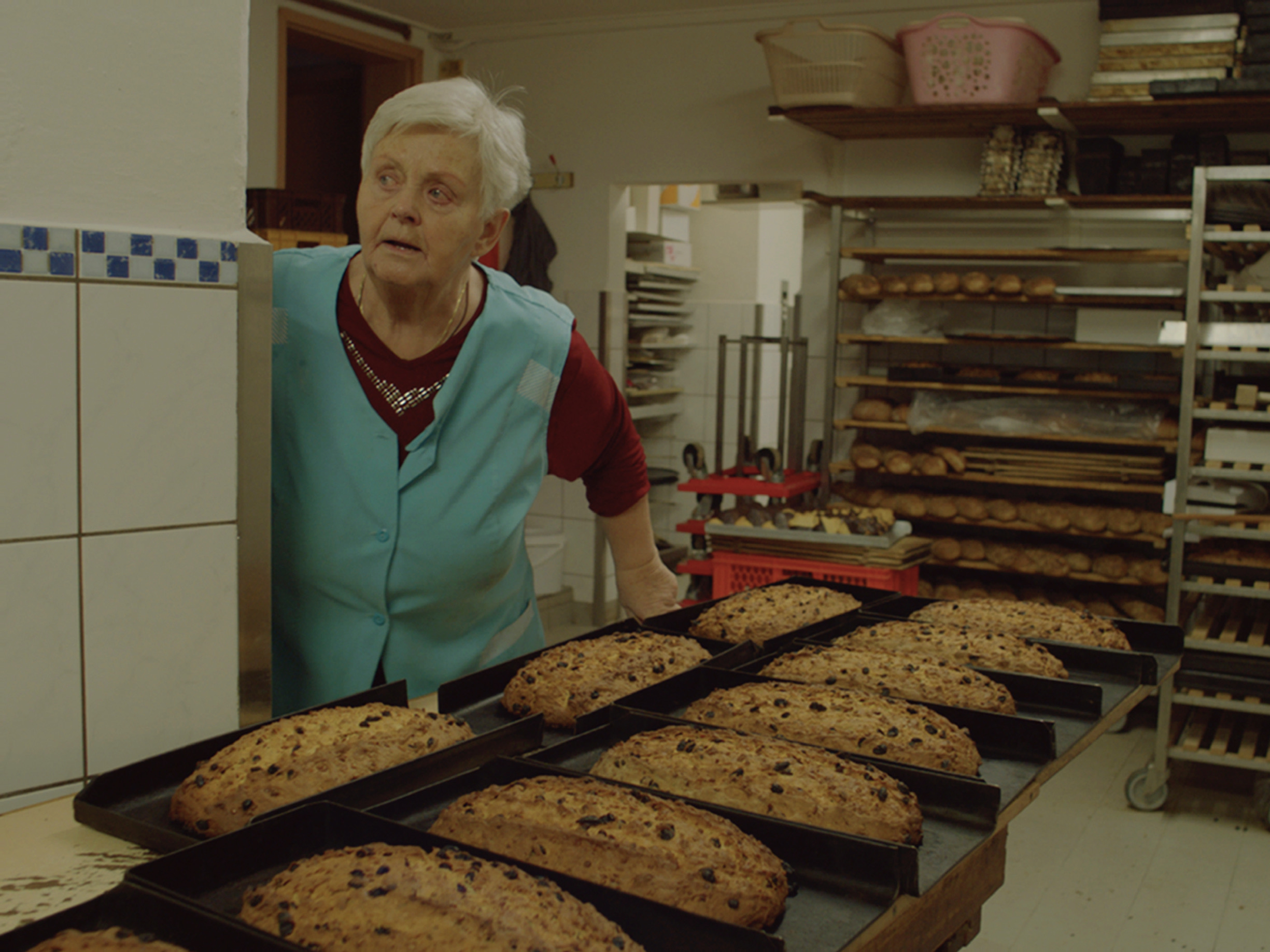 KI generiert: Das Bild zeigt eine Frau in einer Bäckerei, die offenbar gerade Brotlaibe begutachtet. Im Hintergrund sind Regale mit weiteren Backwaren zu sehen.