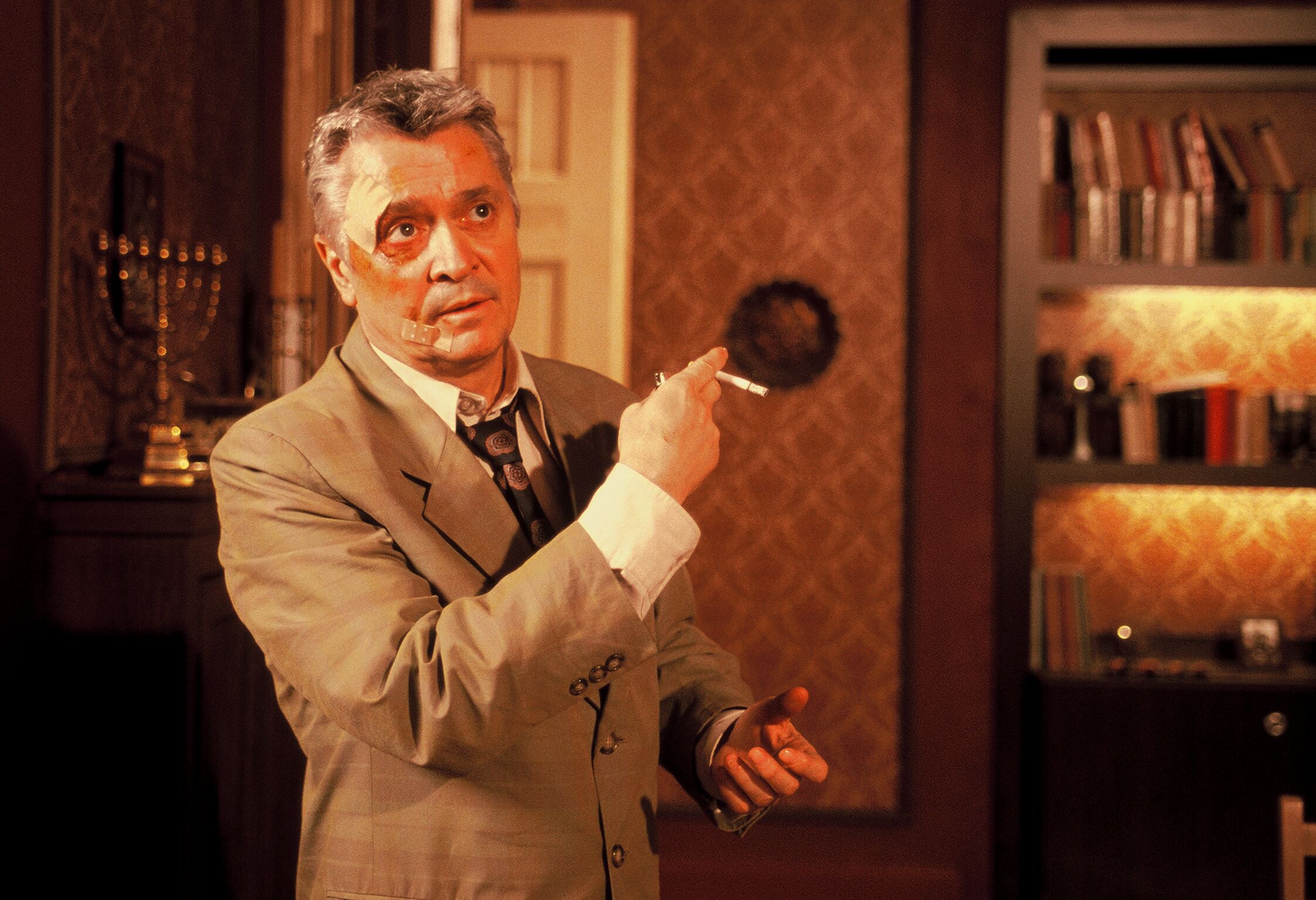 KI generiert: Ein Mann in einem Anzug steht in einem elegant eingerichteten Raum und hält eine Zigarette in der Hand. Im Hintergrund sind Bücherregale und ein dekoratives Element sichtbar.