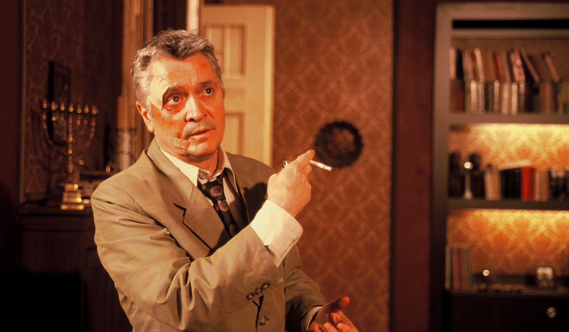 KI generiert: Ein Mann in einem Anzug steht in einem elegant eingerichteten Raum und hält eine Zigarette in der Hand. Im Hintergrund sind Bücherregale und ein dekoratives Element sichtbar.