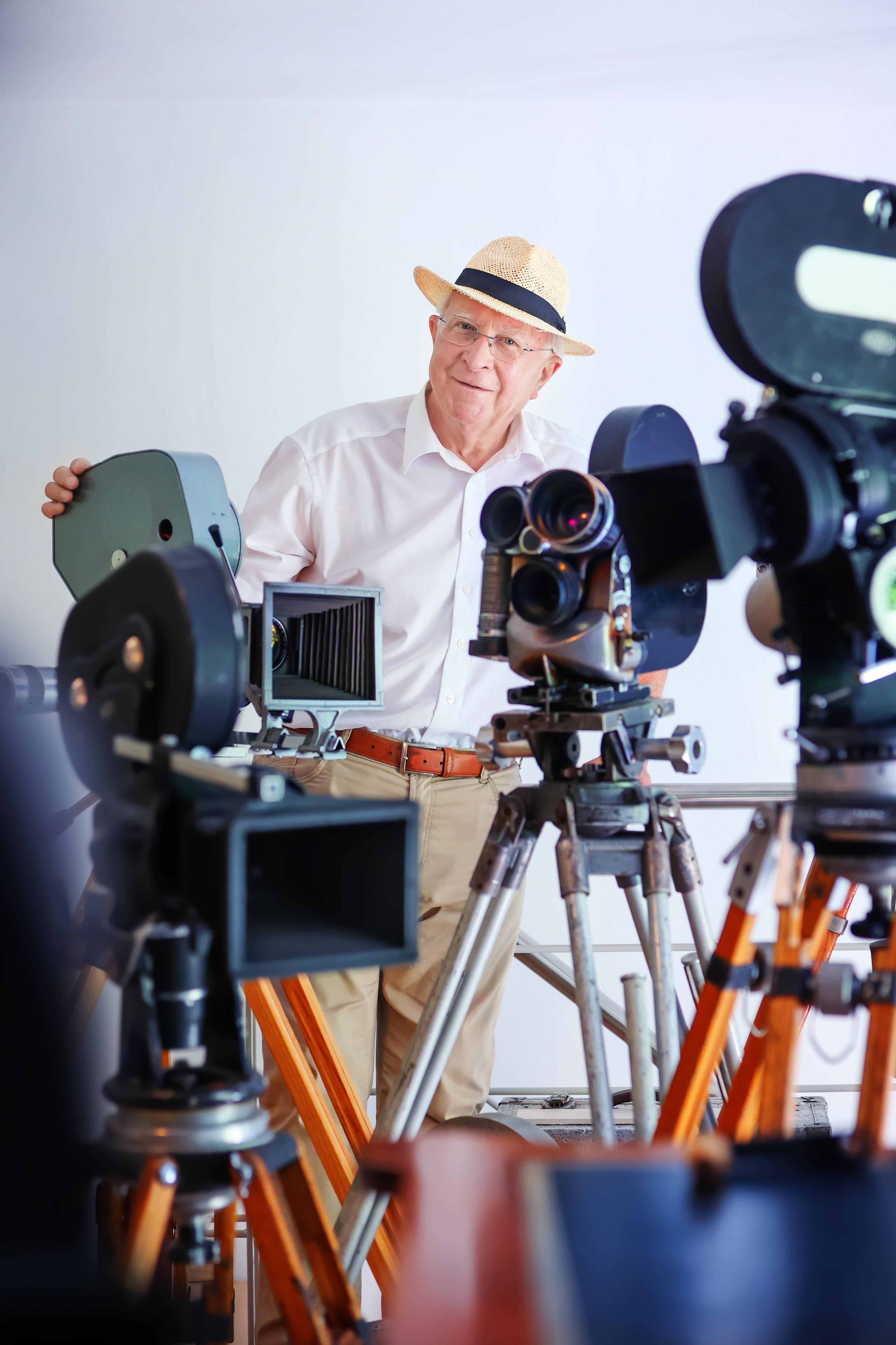 KI generiert: Ein älterer Mann mit Hut steht lächelnd zwischen mehreren alten Filmkameras, die auf Stativen positioniert sind. Der Fokus liegt auf der Sammlung klassischer Filmtechnik.