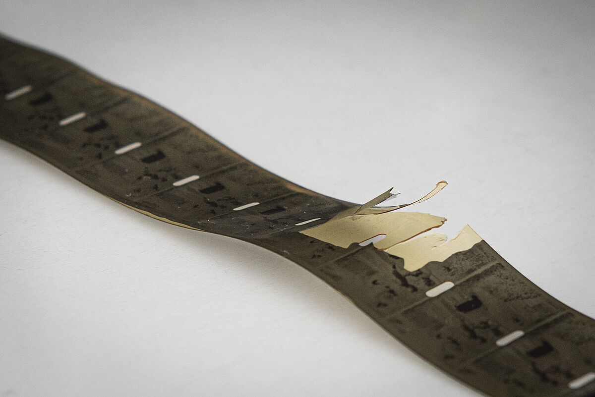 KI generiert: Das Bild zeigt einen beschädigten Filmstreifen, dessen Oberfläche Risse und Abblätterungen aufweist. Der Fokus liegt auf dem physisch beschädigten Zustand des Materials.